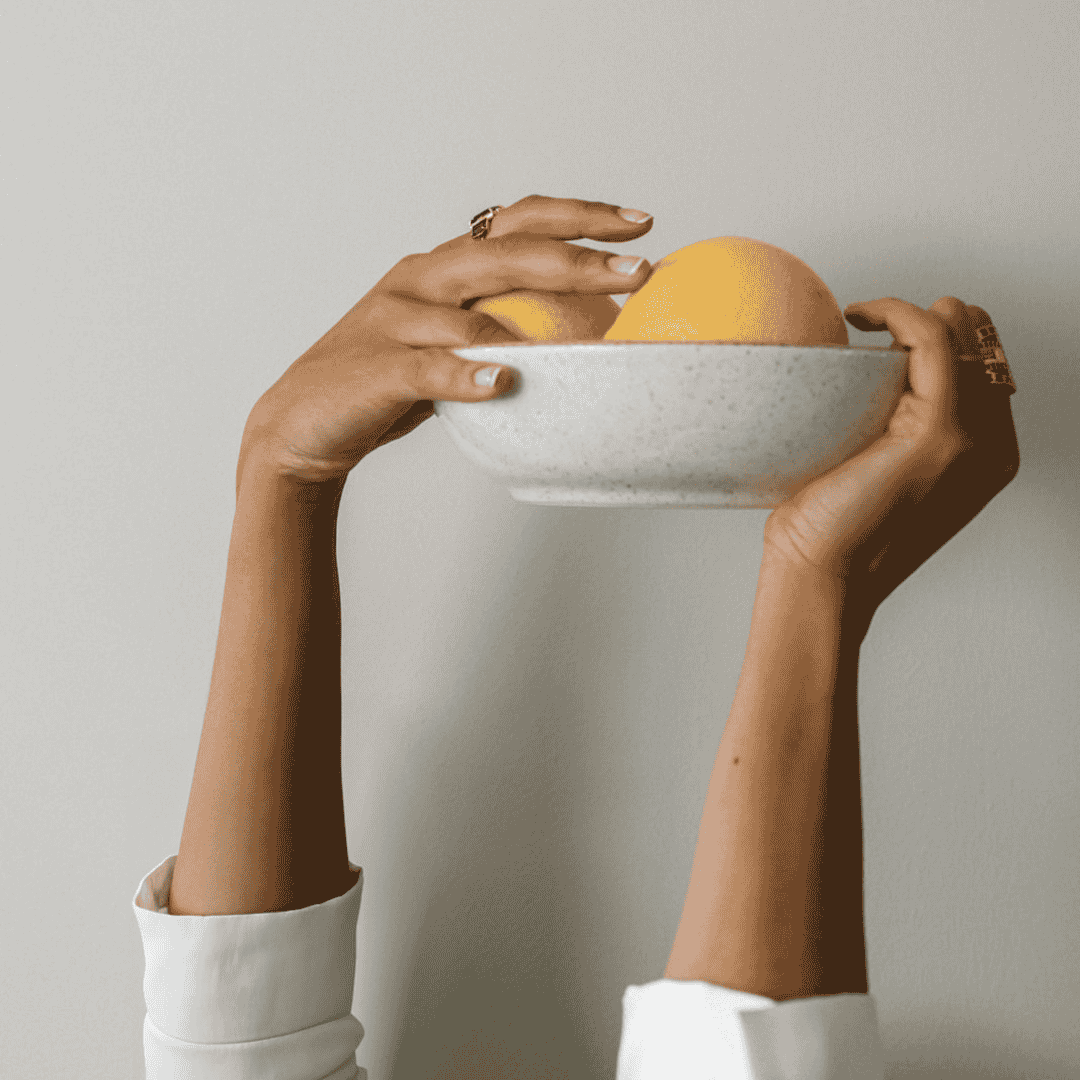 Zoom sur les mains d'une femme qui porte en l'air une coupelle de fruits pour illustrer le soin des ongles par l'alimentation