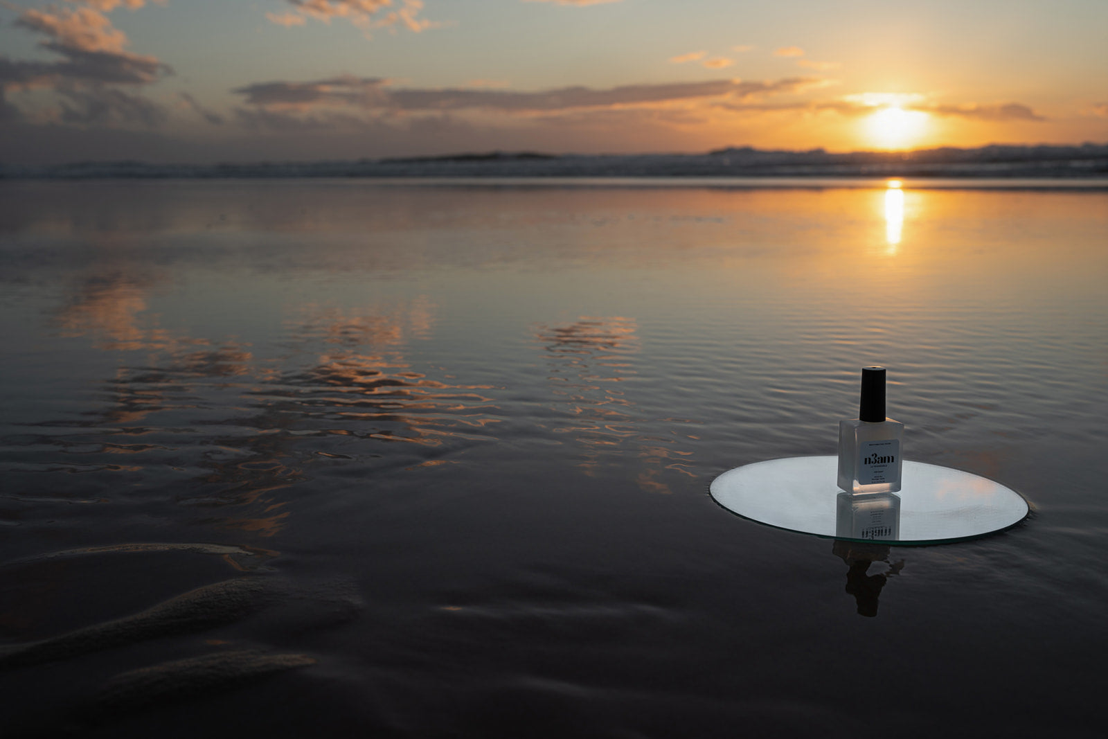 Vernis à ongles perméable transparent posé sur un miroir sur une plage face à un coucher de soleil