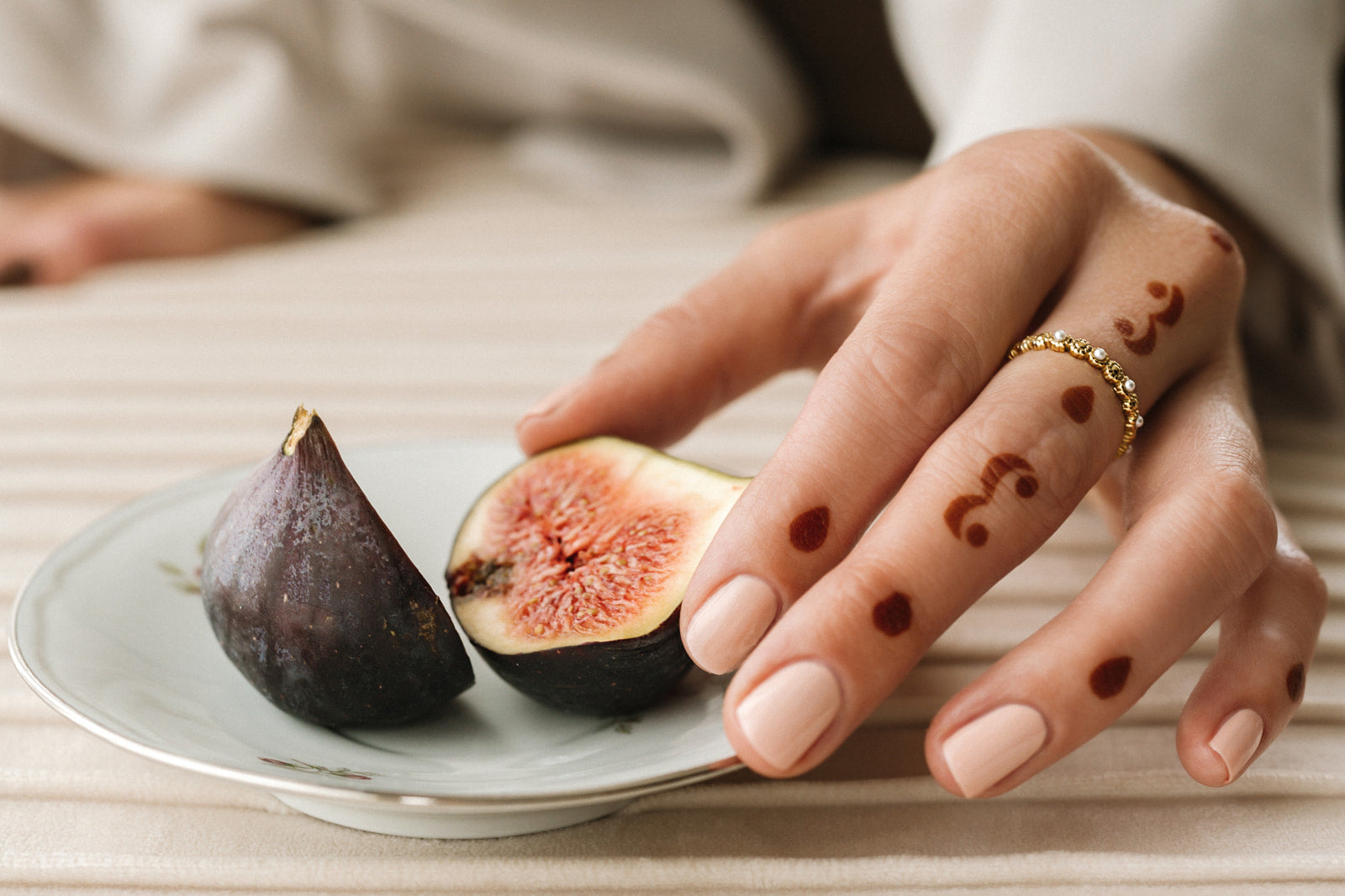 Main d'une femme portant du henné et de vernis perméable nude, elle attrape une figue posée dans une assiette en porcelaine