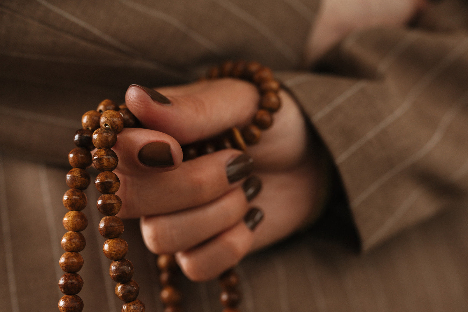 Main d'une femme portant du vernis à ongles perméable marron chocolat tenant un chapelet