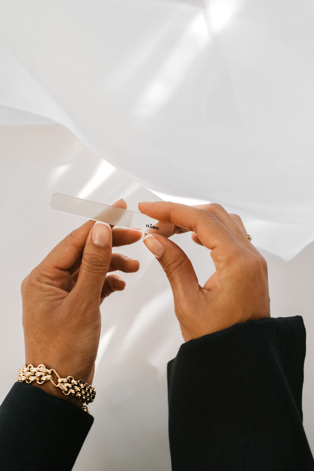 Mains d'une femme portant du une french manucure faite avec du vernis perméable. Elle se lime les ongles avec une lime en verre