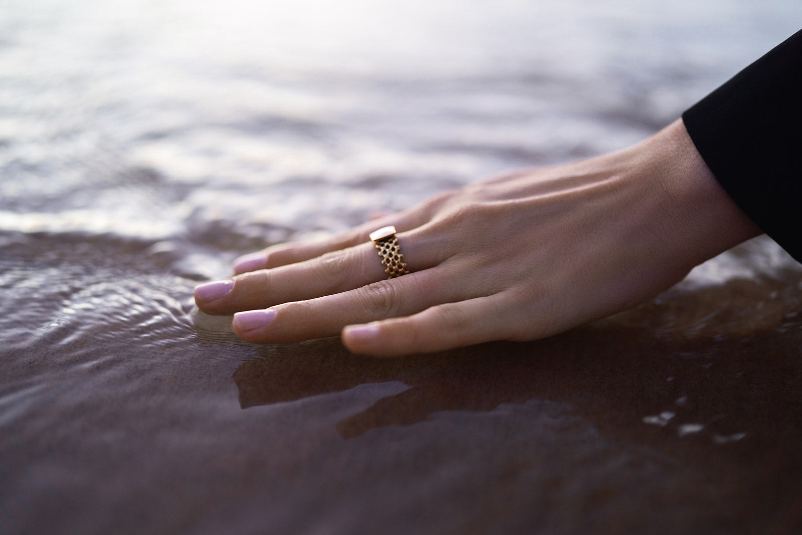 Main d'une femme portant du vernis perméable rose caressant l'eau de la mer